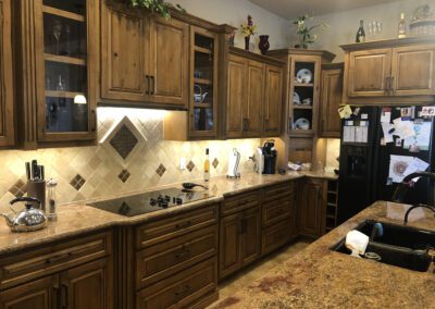 A kitchen with wooden cabinets, granite countertops, tiled backsplash, and various appliances including a stove, toaster, coffee maker, and refrigerator covered with magnets and notes.